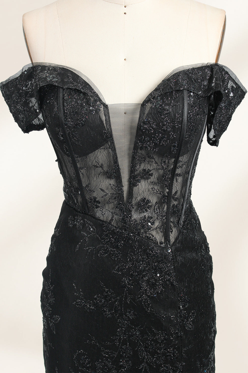 This photograph features a mannequin wearing an elegant, floor-length black lace gown. The gown has a sweetheart neckline, off-the-shoulder sleeves, and a high slit on one side, revealing a black thigh-high stocking. The intricate lace pattern is delicate and ornate, adding texture and visual interest. The mannequin stands against a plain, light beige background, emphasizing the dress's details. The number "2" is displayed on the mannequin's chest.04