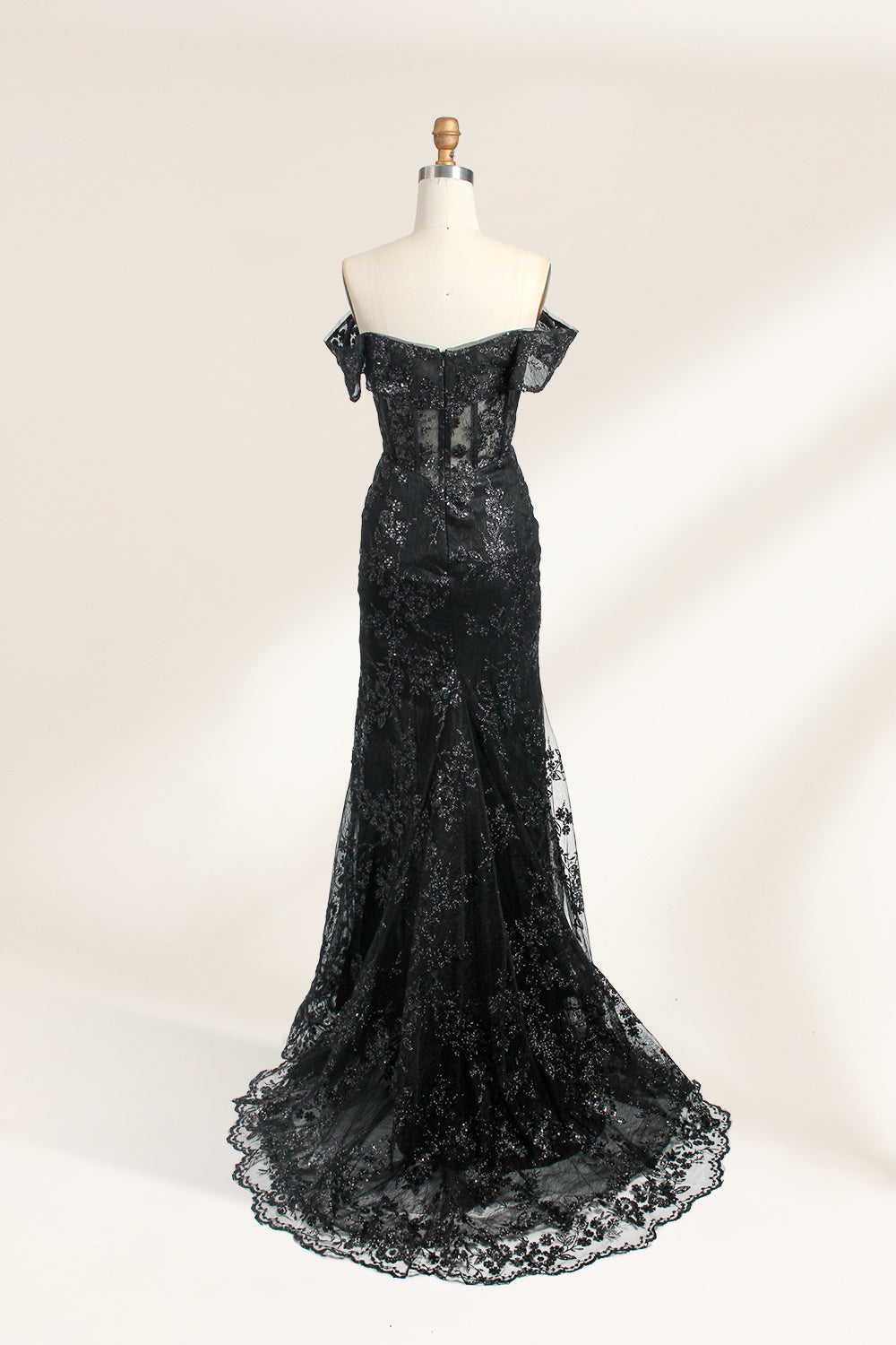 This photograph features a mannequin wearing an elegant, floor-length black lace gown. The gown has a sweetheart neckline, off-the-shoulder sleeves, and a high slit on one side, revealing a black thigh-high stocking. The intricate lace pattern is delicate and ornate, adding texture and visual interest. The mannequin stands against a plain, light beige background, emphasizing the dress's details. The number "2" is displayed on the mannequin's chest.02