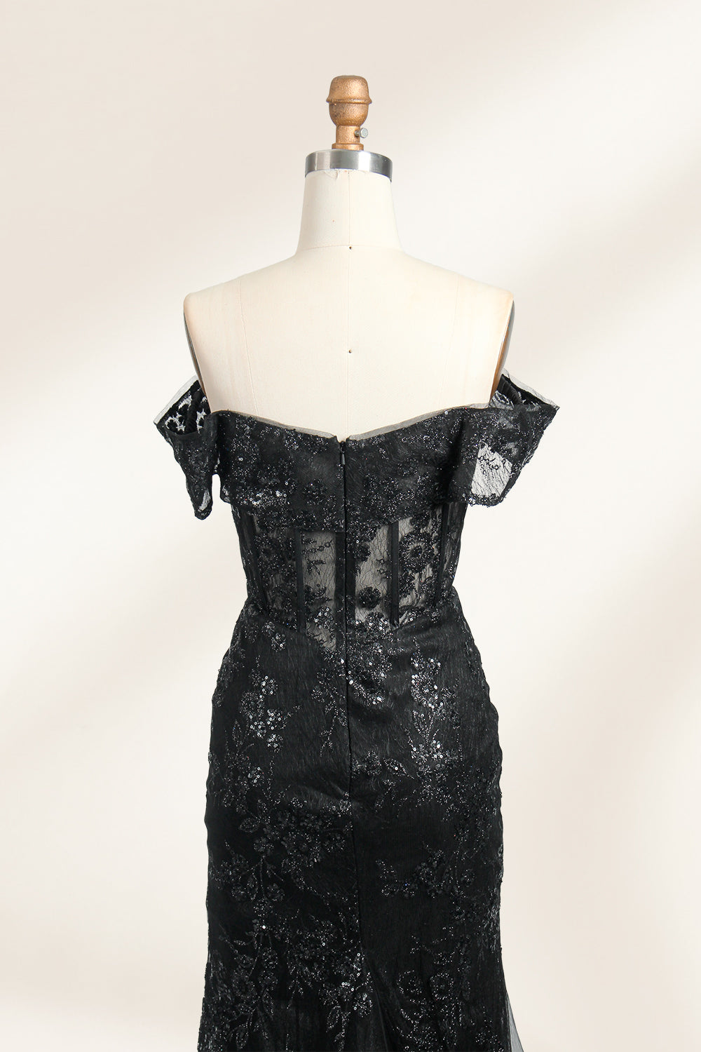 This photograph features a mannequin wearing an elegant, floor-length black lace gown. The gown has a sweetheart neckline, off-the-shoulder sleeves, and a high slit on one side, revealing a black thigh-high stocking. The intricate lace pattern is delicate and ornate, adding texture and visual interest. The mannequin stands against a plain, light beige background, emphasizing the dress's details. The number "2" is displayed on the mannequin's chest.06