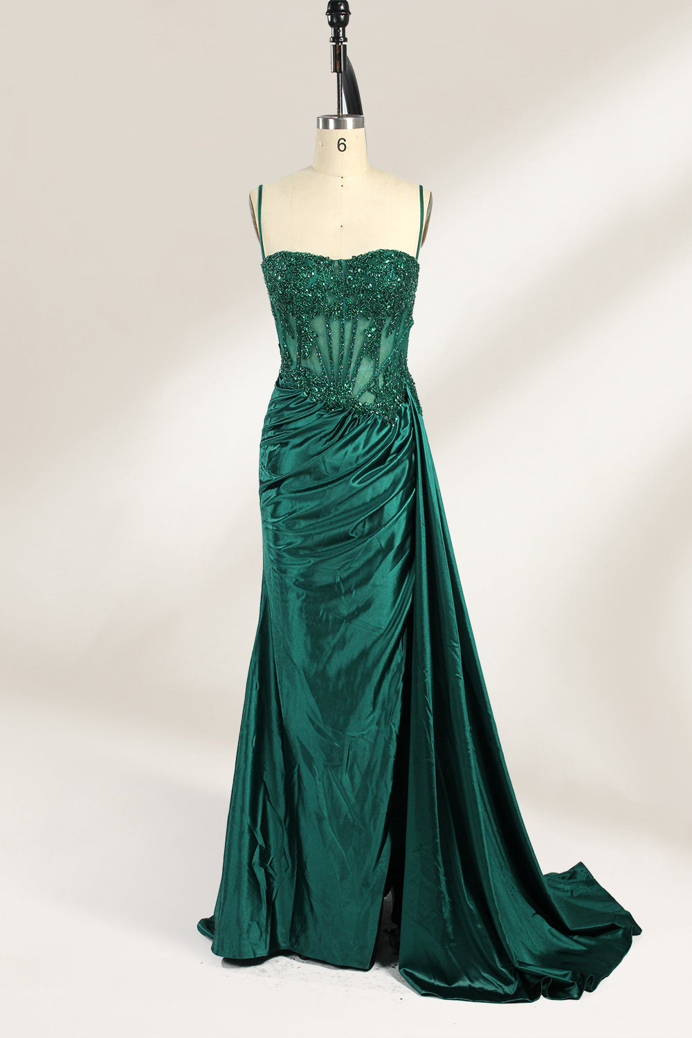 Photograph of an elegant, strapless green satin evening gown on a dress form. The dress features a fitted bodice adorned with intricate beading and lacework, transitioning into a flowing, ruched skirt that cascades to the floor. The gown's deep emerald green color exudes luxury and sophistication. The background is a plain, off-white studio setting, highlighting the dress's opulence. The dress form is positioned centrally, with the dress's front view prominently displayed.1