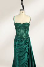 Photograph of an elegant, strapless green satin evening gown on a dress form. The dress features a fitted bodice adorned with intricate beading and lacework, transitioning into a flowing, ruched skirt that cascades to the floor. The gown's deep emerald green color exudes luxury and sophistication. The background is a plain, off-white studio setting, highlighting the dress's opulence. The dress form is positioned centrally, with the dress's front view prominently displayed.5