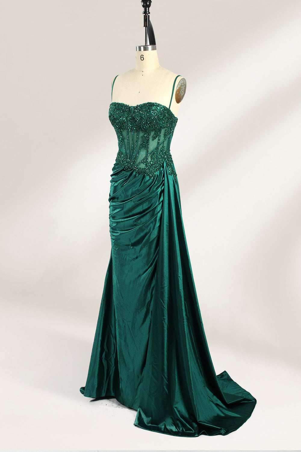 Photograph of an elegant, strapless green satin evening gown on a dress form. The dress features a fitted bodice adorned with intricate beading and lacework, transitioning into a flowing, ruched skirt that cascades to the floor. The gown's deep emerald green color exudes luxury and sophistication. The background is a plain, off-white studio setting, highlighting the dress's opulence. The dress form is positioned centrally, with the dress's front view prominently displayed.6