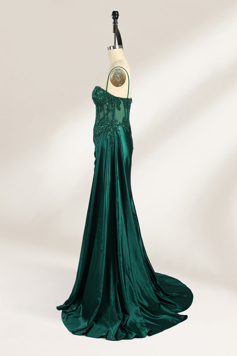 Photograph of an elegant, strapless green satin evening gown on a dress form. The dress features a fitted bodice adorned with intricate beading and lacework, transitioning into a flowing, ruched skirt that cascades to the floor. The gown's deep emerald green color exudes luxury and sophistication. The background is a plain, off-white studio setting, highlighting the dress's opulence. The dress form is positioned centrally, with the dress's front view prominently displayed.4