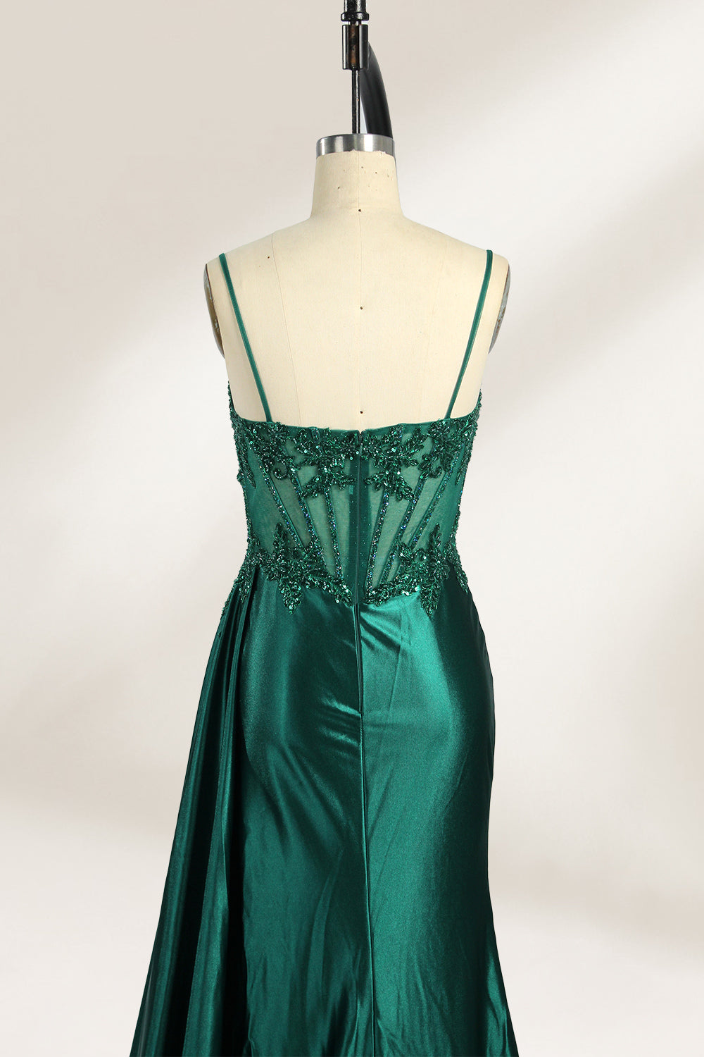 Photograph of an elegant, strapless green satin evening gown on a dress form. The dress features a fitted bodice adorned with intricate beading and lacework, transitioning into a flowing, ruched skirt that cascades to the floor. The gown's deep emerald green color exudes luxury and sophistication. The background is a plain, off-white studio setting, highlighting the dress's opulence. The dress form is positioned centrally, with the dress's front view prominently displayed.3