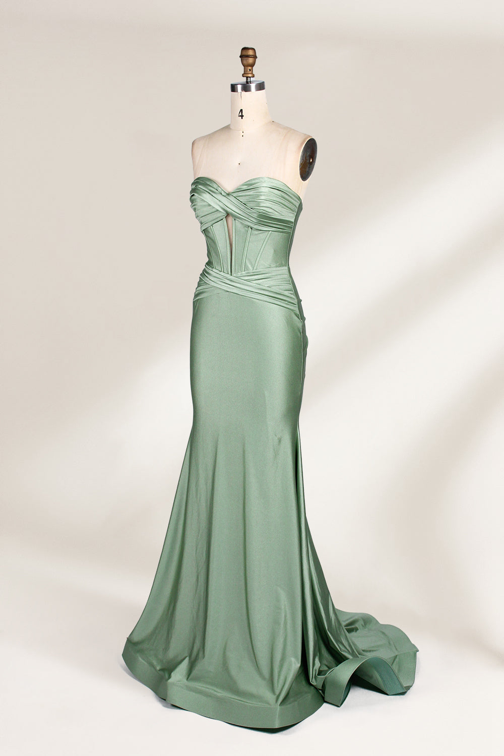 This photograph showcases a floor-length, strapless gown in a soft, mint green hue. The dress features a fitted bodice with a sweetheart neckline and a delicate, crisscrossed fabric pattern, accentuating the bust. The skirt flares out elegantly, ending in a subtle train. The gown is displayed on a mannequin with a wooden head and neck, set against a plain, light beige background. The fabric appears to be satin or silk, giving it a smooth, lustrous texture. 4