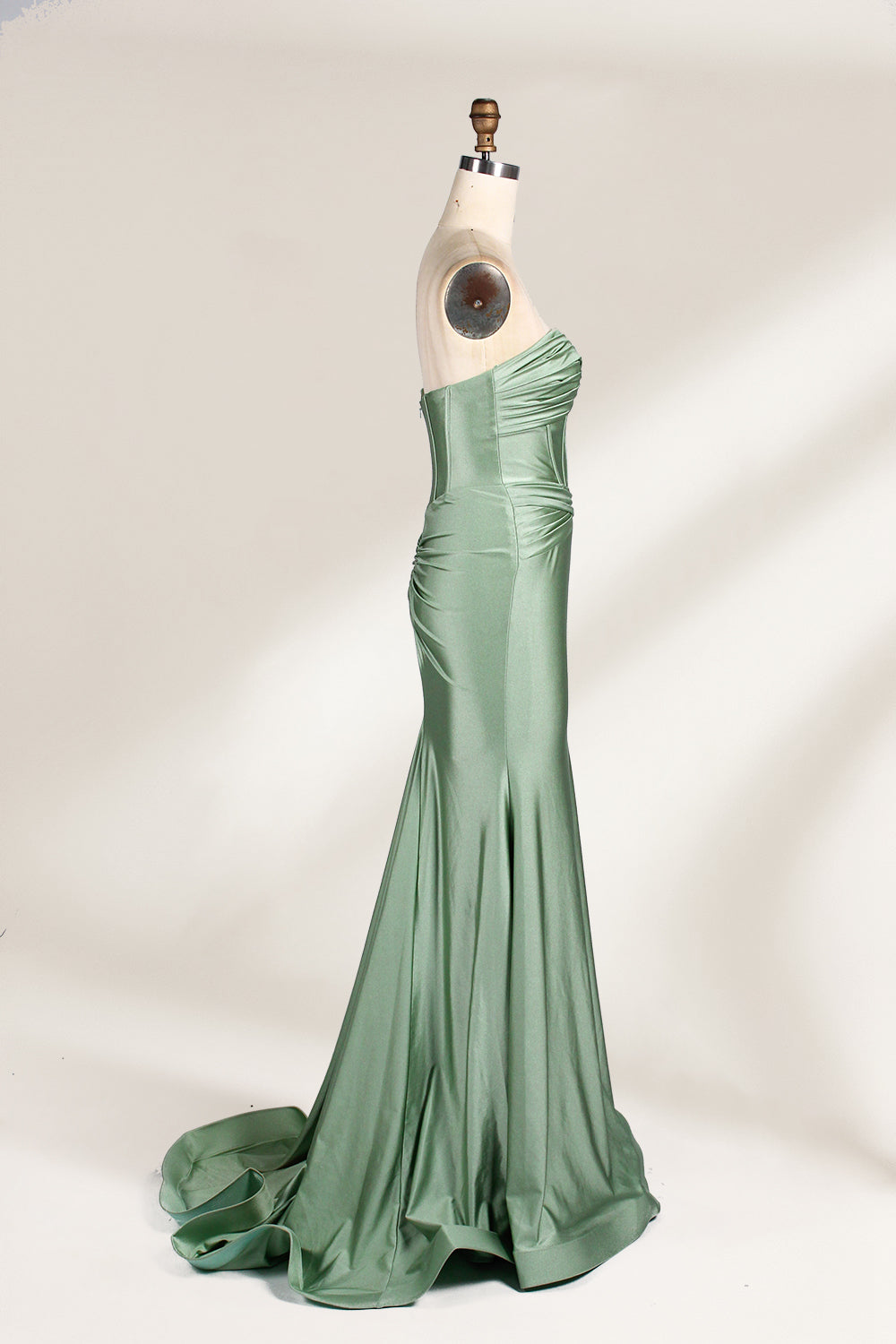 This photograph showcases a floor-length, strapless gown in a soft, mint green hue. The dress features a fitted bodice with a sweetheart neckline and a delicate, crisscrossed fabric pattern, accentuating the bust. The skirt flares out elegantly, ending in a subtle train. The gown is displayed on a mannequin with a wooden head and neck, set against a plain, light beige background. The fabric appears to be satin or silk, giving it a smooth, lustrous texture. 5