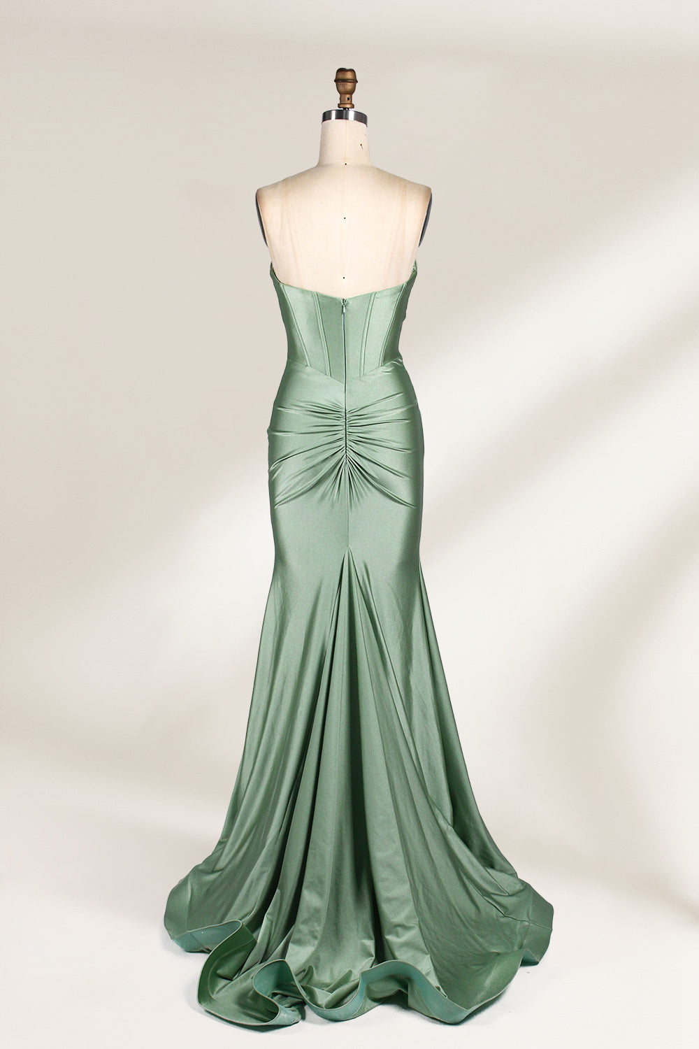 This photograph showcases a floor-length, strapless gown in a soft, mint green hue. The dress features a fitted bodice with a sweetheart neckline and a delicate, crisscrossed fabric pattern, accentuating the bust. The skirt flares out elegantly, ending in a subtle train. The gown is displayed on a mannequin with a wooden head and neck, set against a plain, light beige background. The fabric appears to be satin or silk, giving it a smooth, lustrous texture. 2