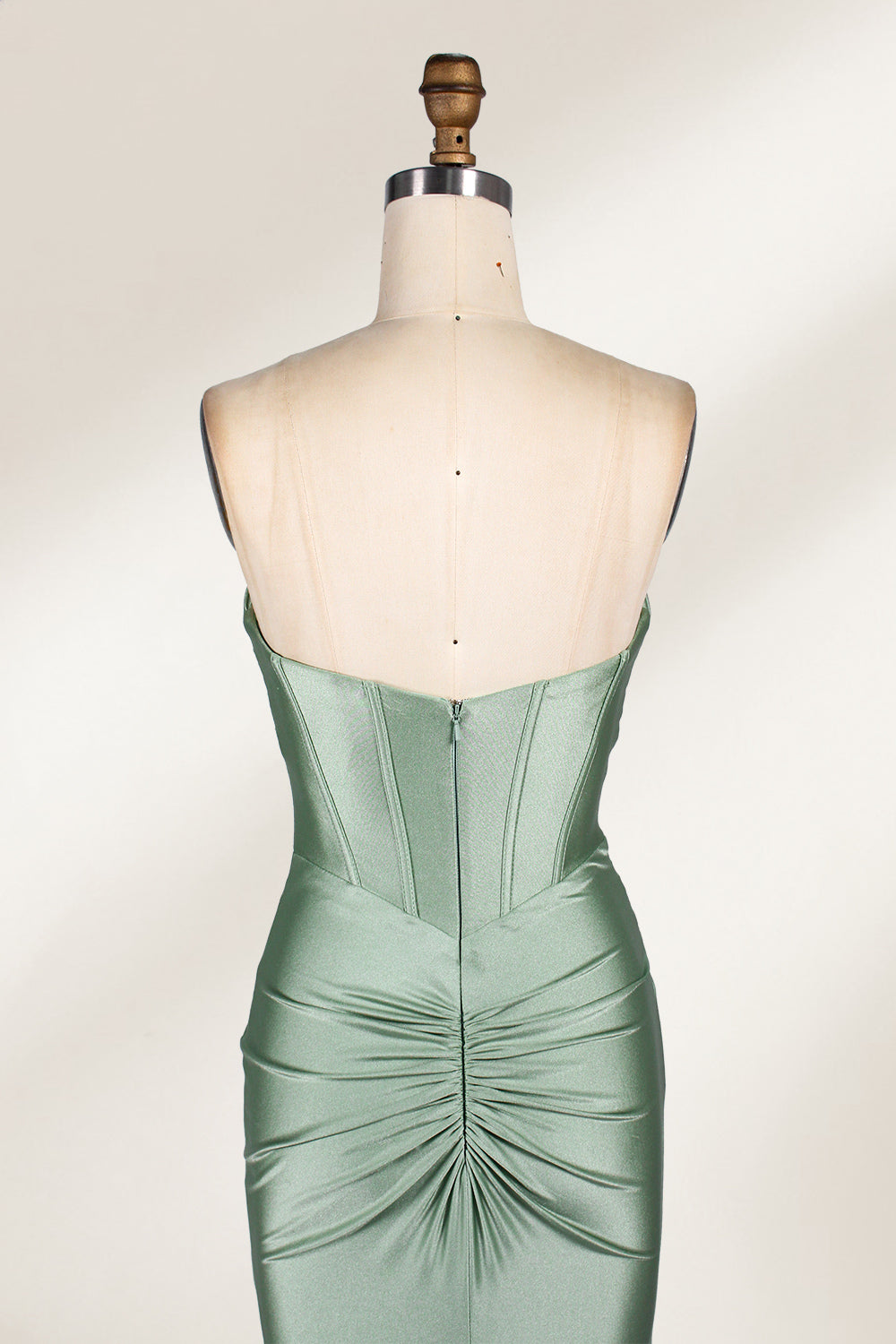This photograph showcases a floor-length, strapless gown in a soft, mint green hue. The dress features a fitted bodice with a sweetheart neckline and a delicate, crisscrossed fabric pattern, accentuating the bust. The skirt flares out elegantly, ending in a subtle train. The gown is displayed on a mannequin with a wooden head and neck, set against a plain, light beige background. The fabric appears to be satin or silk, giving it a smooth, lustrous texture. 6