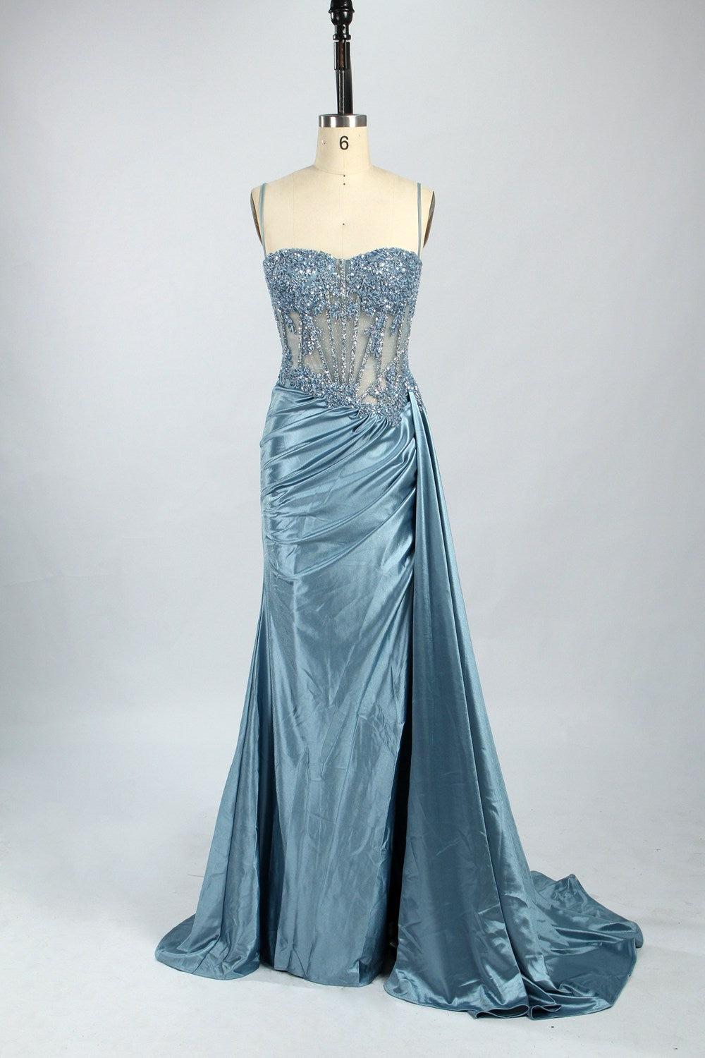 Photograph of an elegant, strapless green satin evening gown on a dress form. The dress features a fitted bodice adorned with intricate beading and lacework, transitioning into a flowing, ruched skirt that cascades to the floor. The gown's deep emerald green color exudes luxury and sophistication. The background is a plain, off-white studio setting, highlighting the dress's opulence. The dress form is positioned centrally, with the dress's front view prominently displayed.7