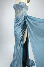 Photograph of an elegant, strapless green satin evening gown on a dress form. The dress features a fitted bodice adorned with intricate beading and lacework, transitioning into a flowing, ruched skirt that cascades to the floor. The gown's deep emerald green color exudes luxury and sophistication. The background is a plain, off-white studio setting, highlighting the dress's opulence. The dress form is positioned centrally, with the dress's front view prominently displayed.8