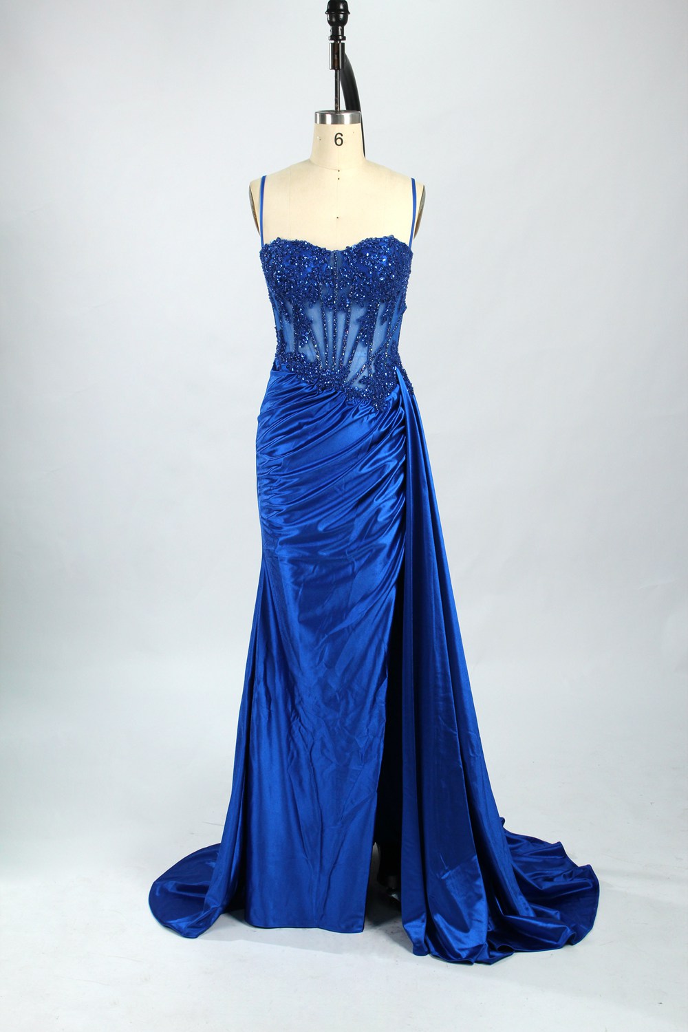 Photograph of an elegant, strapless green satin evening gown on a dress form. The dress features a fitted bodice adorned with intricate beading and lacework, transitioning into a flowing, ruched skirt that cascades to the floor. The gown's deep emerald green color exudes luxury and sophistication. The background is a plain, off-white studio setting, highlighting the dress's opulence. The dress form is positioned centrally, with the dress's front view prominently displayed.9