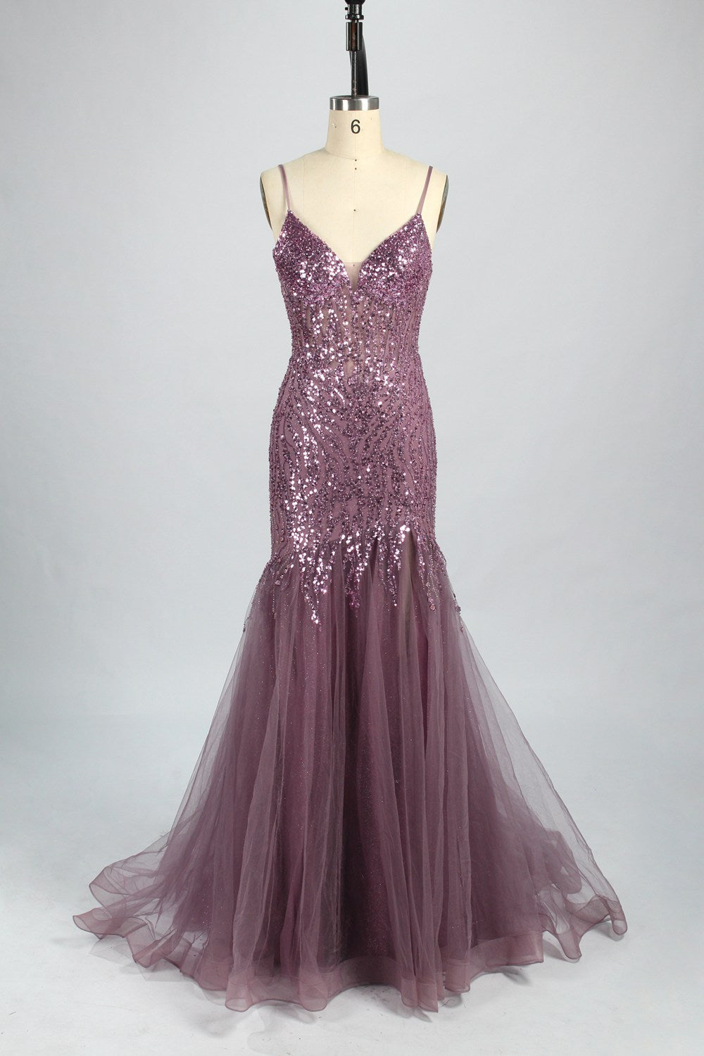 Photograph of a young Asian woman with fair skin and dark hair in a sleek bun, wearing a stunning, floor-length, deep blue evening gown. The gown has a plunging V-neckline, adorned with intricate beading and sequins, and features a sheer overlay with a high slit on one side, revealing a layer of tulle. The background is a soft, neutral gradient, highlighting the gown's elegance. She accessorizes with large, dangling earrings.7