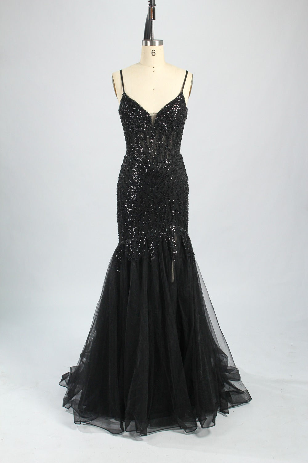 Photograph of a young Asian woman with fair skin and dark hair in a sleek bun, wearing a stunning, floor-length, deep blue evening gown. The gown has a plunging V-neckline, adorned with intricate beading and sequins, and features a sheer overlay with a high slit on one side, revealing a layer of tulle. The background is a soft, neutral gradient, highlighting the gown's elegance. She accessorizes with large, dangling earrings.8