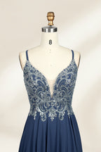 Photograph of a mannequin showcasing an elegant, floor-length evening gown. The gown features a deep V-neckline adorned with intricate blue floral embroidery, transitioning into a flowing, dark blue chiffon skirt. The mannequin stands against a plain, cream-colored backdrop. The dress exudes sophistication and luxury, perfect for formal events.03