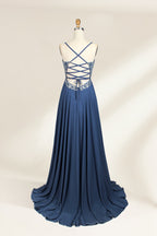 Photograph of a mannequin showcasing an elegant, floor-length evening gown. The gown features a deep V-neckline adorned with intricate blue floral embroidery, transitioning into a flowing, dark blue chiffon skirt. The mannequin stands against a plain, cream-colored backdrop. The dress exudes sophistication and luxury, perfect for formal events.