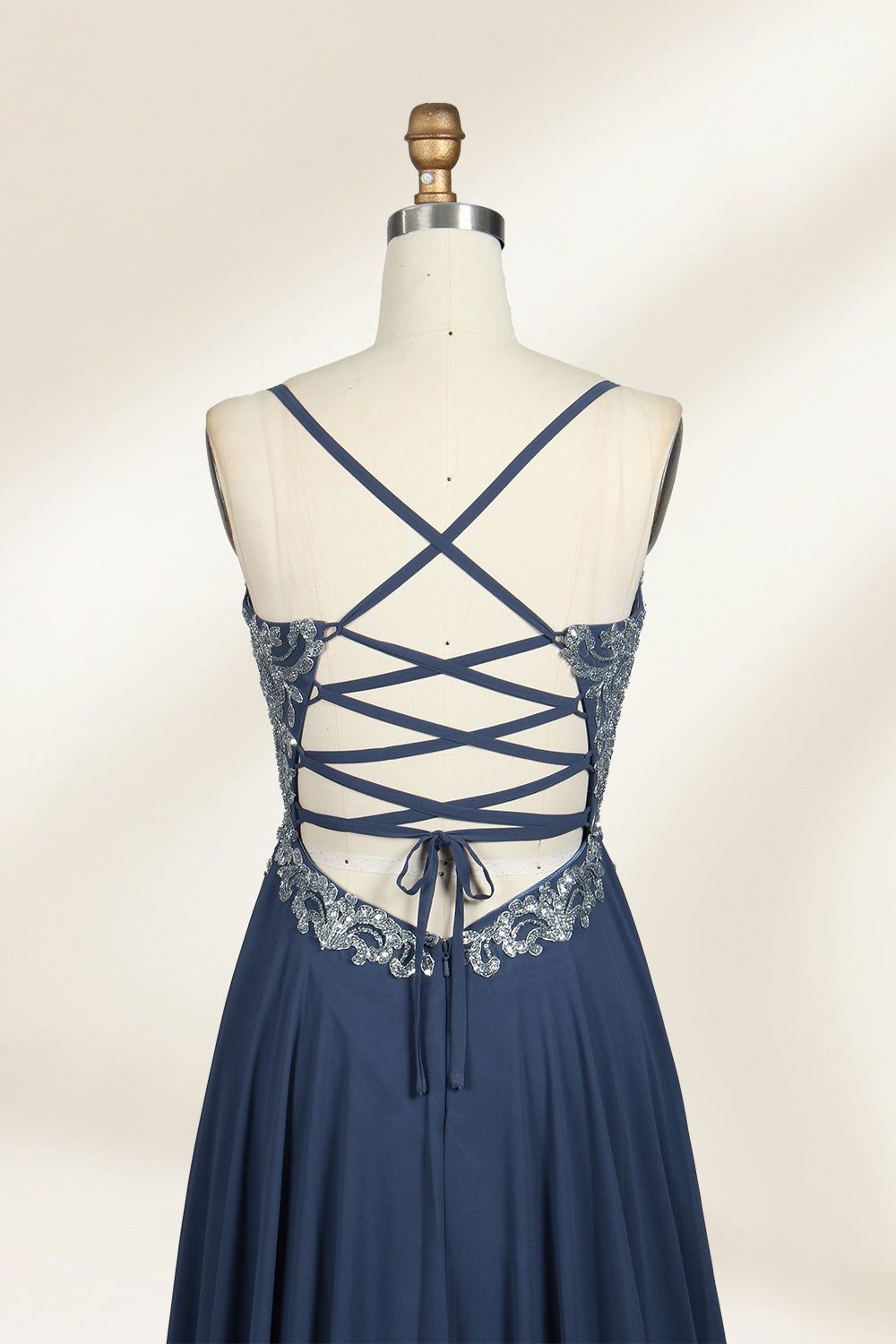 Photograph of a mannequin showcasing an elegant, floor-length evening gown. The gown features a deep V-neckline adorned with intricate blue floral embroidery, transitioning into a flowing, dark blue chiffon skirt. The mannequin stands against a plain, cream-colored backdrop. The dress exudes sophistication and luxury, perfect for formal events.06