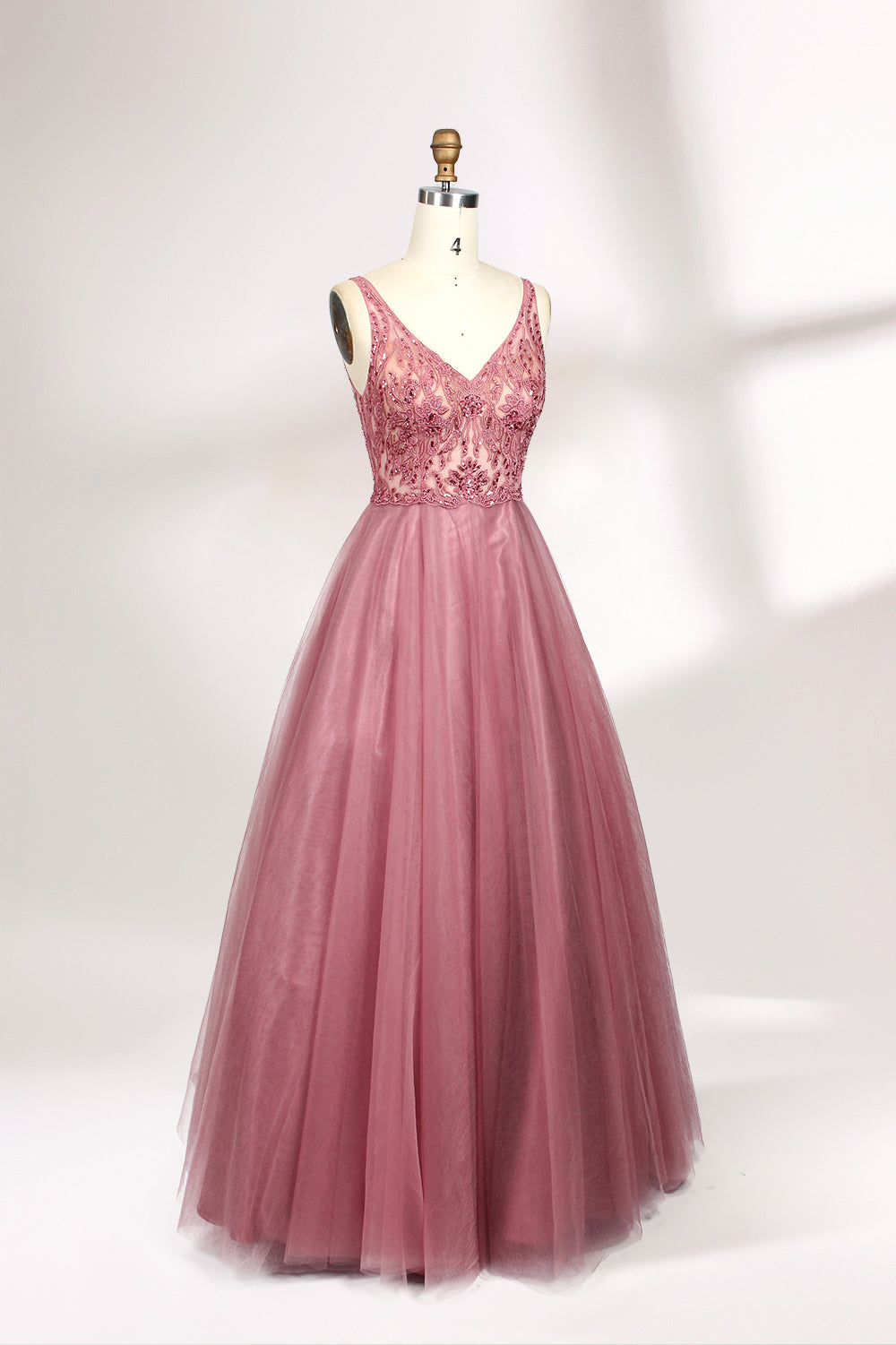 Photograph of a mannequin showcasing a floor-length, sleeveless, pink tulle gown with intricate lace detailing on the bodice and neckline. The gown features a fitted waist and flares out into a voluminous skirt, creating a ballerina-style silhouette. The mannequin stands against a plain white background with soft, diffused lighting casting subtle shadows.03
