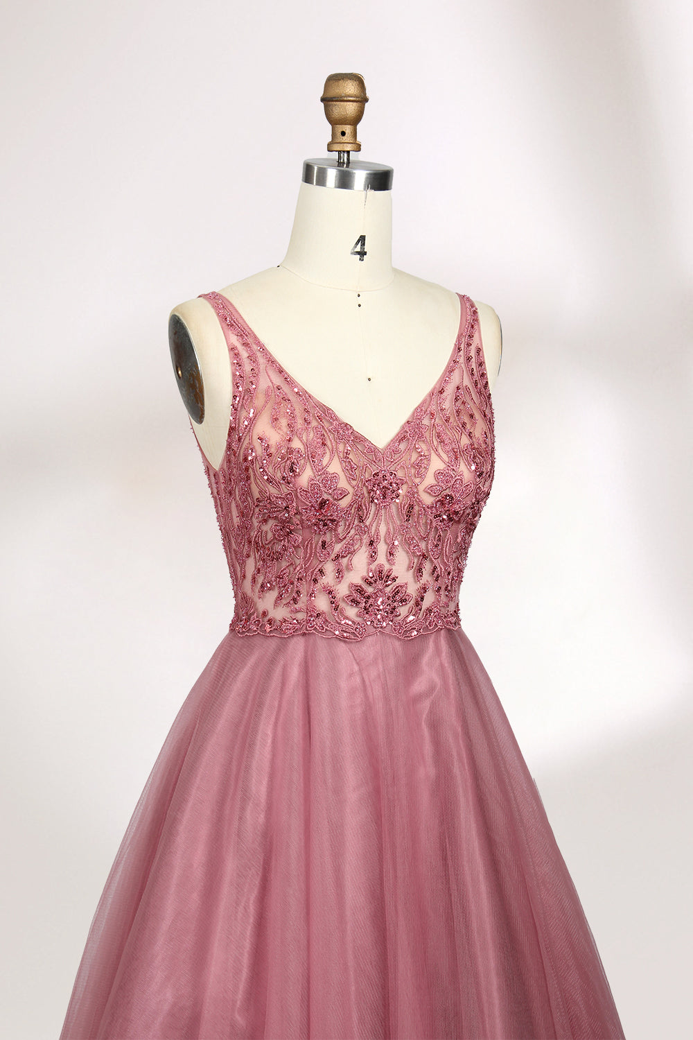 Photograph of a mannequin showcasing a floor-length, sleeveless, pink tulle gown with intricate lace detailing on the bodice and neckline. The gown features a fitted waist and flares out into a voluminous skirt, creating a ballerina-style silhouette. The mannequin stands against a plain white background with soft, diffused lighting casting subtle shadows.04
