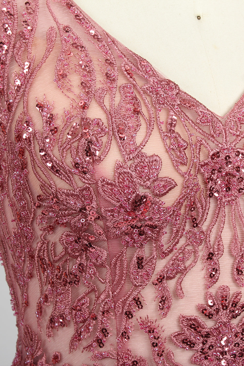 Photograph of a mannequin showcasing a floor-length, sleeveless, pink tulle gown with intricate lace detailing on the bodice and neckline. The gown features a fitted waist and flares out into a voluminous skirt, creating a ballerina-style silhouette. The mannequin stands against a plain white background with soft, diffused lighting casting subtle shadows.05