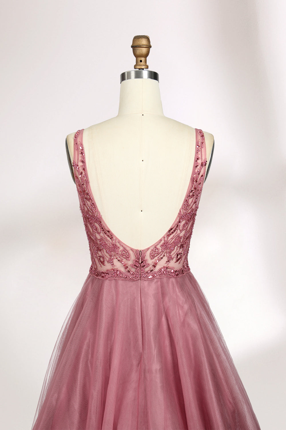 Photograph of a mannequin showcasing a floor-length, sleeveless, pink tulle gown with intricate lace detailing on the bodice and neckline. The gown features a fitted waist and flares out into a voluminous skirt, creating a ballerina-style silhouette. The mannequin stands against a plain white background with soft, diffused lighting casting subtle shadows.06