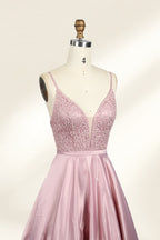 Photograph of a stylish, sleeveless, floor-length satin gown on a dress form. The dress features a deep V-neckline adorned with intricate lace, and a high-waisted bodice that flares into a voluminous skirt. The gown is a soft, blush pink color. The background is a plain, light beige, enhancing the dress's elegant design.023