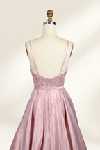 Photograph of a stylish, sleeveless, floor-length satin gown on a dress form. The dress features a deep V-neckline adorned with intricate lace, and a high-waisted bodice that flares into a voluminous skirt. The gown is a soft, blush pink color. The background is a plain, light beige, enhancing the dress's elegant design.06