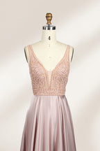 Photograph of a sleeveless, floor-length evening gown displayed on a dress form. The gown features a deep V-neckline adorned with intricate lace detailing and a sheer, blush pink fabric that flows into a smooth, satin skirt. The dress form is positioned against a plain, light beige background, emphasizing the gown's elegant design.03