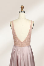 Photograph of a sleeveless, floor-length evening gown displayed on a dress form. The gown features a deep V-neckline adorned with intricate lace detailing and a sheer, blush pink fabric that flows into a smooth, satin skirt. The dress form is positioned against a plain, light beige background, emphasizing the gown's elegant design.06