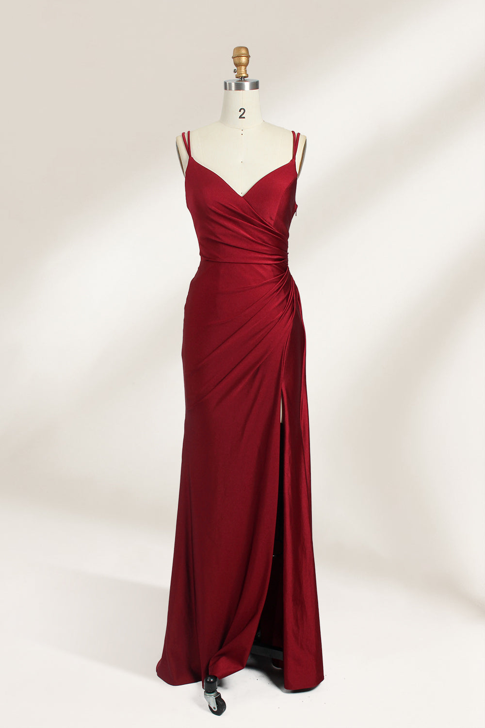 This is a burgundy satin evening gown displayed on a mannequin. It features a sweetheart neckline and thin shoulder straps. The dress has a ruched design along the bodice and waist, accentuating the figure, and a high side slit that adds an elegant, modern touch. The smooth satin fabric gives it a luxurious sheen, making it suitable for formal events like galas or weddings.01