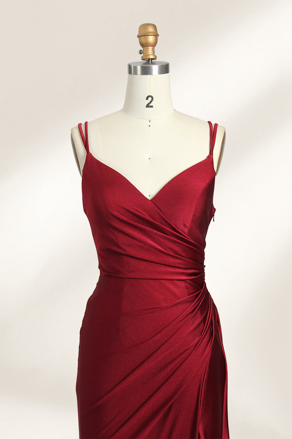 This is a burgundy satin evening gown displayed on a mannequin. It features a sweetheart neckline and thin shoulder straps. The dress has a ruched design along the bodice and waist, accentuating the figure, and a high side slit that adds an elegant, modern touch. The smooth satin fabric gives it a luxurious sheen, making it suitable for formal events like galas or weddings.03