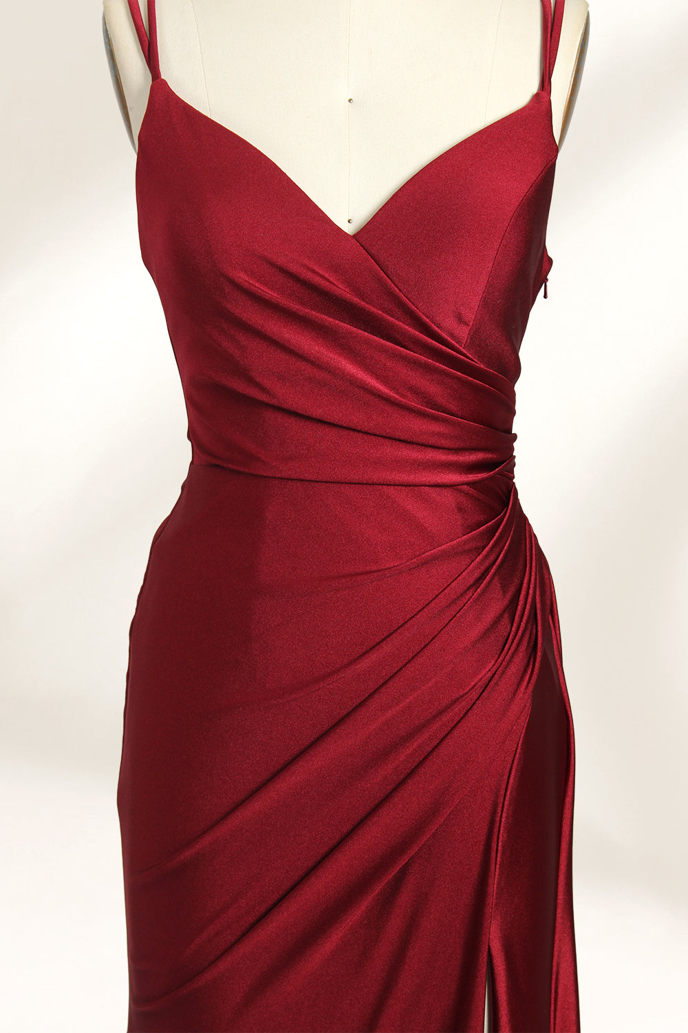 This is a burgundy satin evening gown displayed on a mannequin. It features a sweetheart neckline and thin shoulder straps. The dress has a ruched design along the bodice and waist, accentuating the figure, and a high side slit that adds an elegant, modern touch. The smooth satin fabric gives it a luxurious sheen, making it suitable for formal events like galas or weddings.06