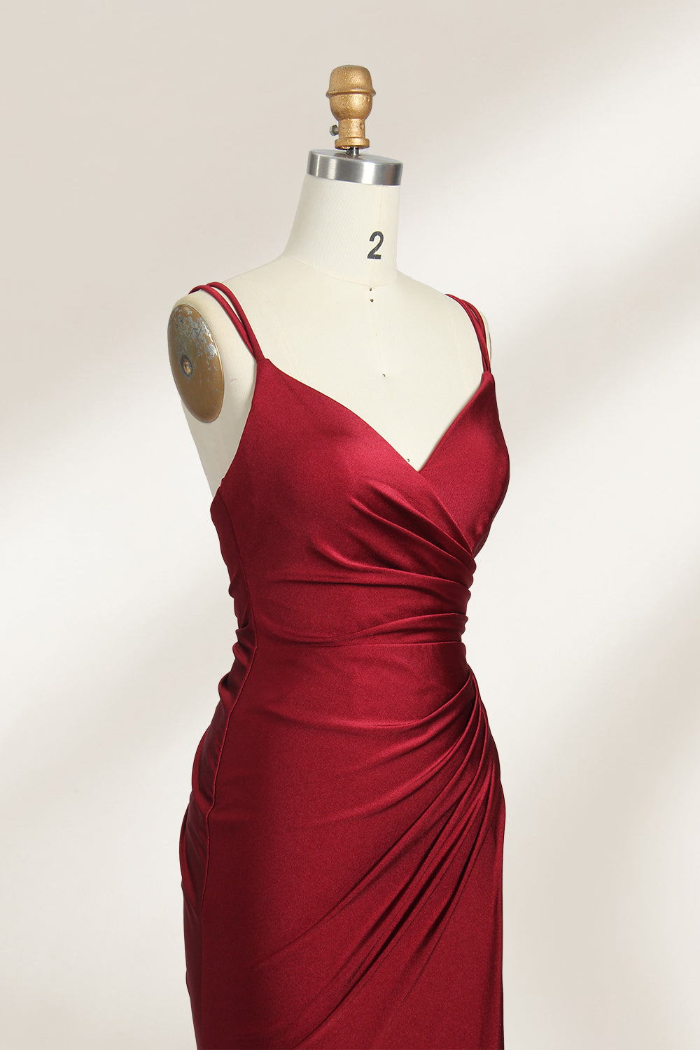 This is a burgundy satin evening gown displayed on a mannequin. It features a sweetheart neckline and thin shoulder straps. The dress has a ruched design along the bodice and waist, accentuating the figure, and a high side slit that adds an elegant, modern touch. The smooth satin fabric gives it a luxurious sheen, making it suitable for formal events like galas or weddings.04
