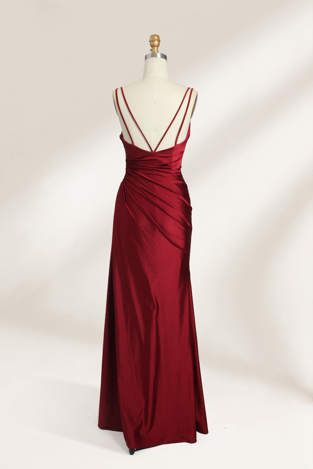 This is a burgundy satin evening gown displayed on a mannequin. It features a sweetheart neckline and thin shoulder straps. The dress has a ruched design along the bodice and waist, accentuating the figure, and a high side slit that adds an elegant, modern touch. The smooth satin fabric gives it a luxurious sheen, making it suitable for formal events like galas or weddings.02