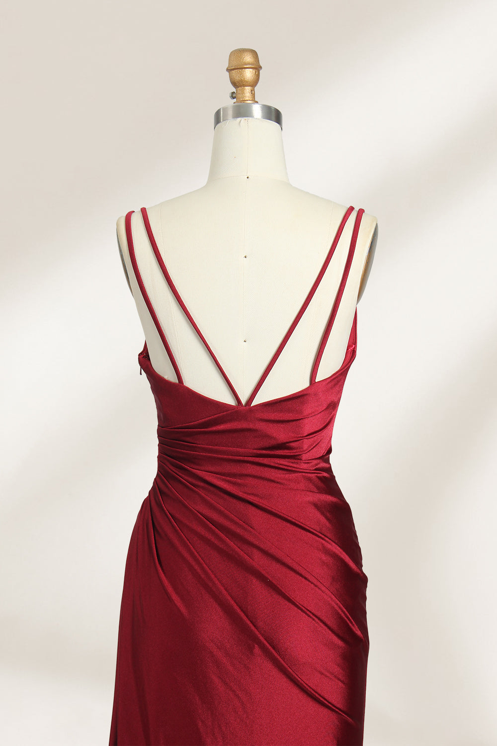 This is a burgundy satin evening gown displayed on a mannequin. It features a sweetheart neckline and thin shoulder straps. The dress has a ruched design along the bodice and waist, accentuating the figure, and a high side slit that adds an elegant, modern touch. The smooth satin fabric gives it a luxurious sheen, making it suitable for formal events like galas or weddings.05