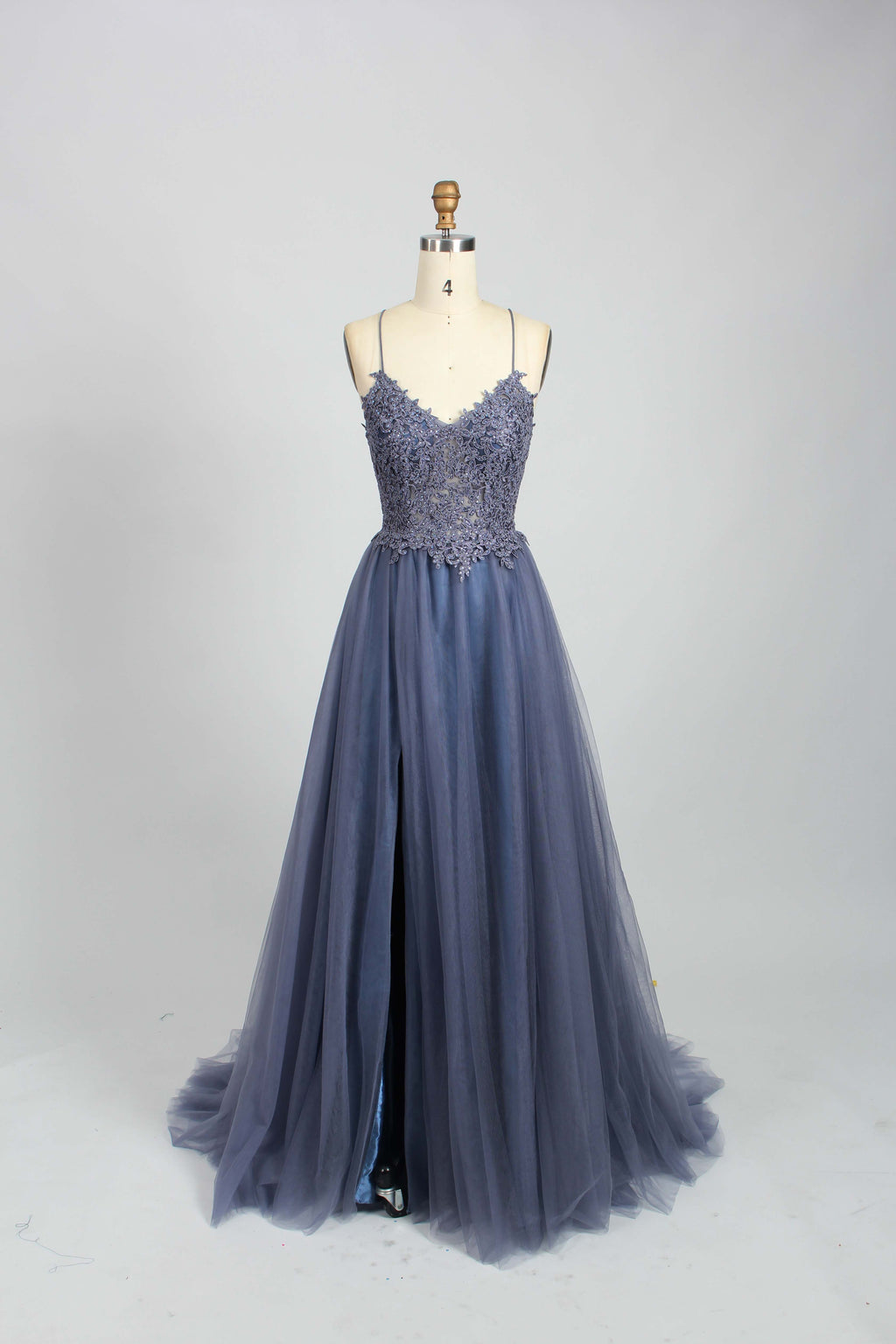 A mannequin showcases a dark - green tulle gown. It has thin spaghetti straps, a lace - detailed bodice, and a voluminous, flowing skirt. The elegant design, with its romantic tulle and delicate lace, suits formal events like galas or weddings.