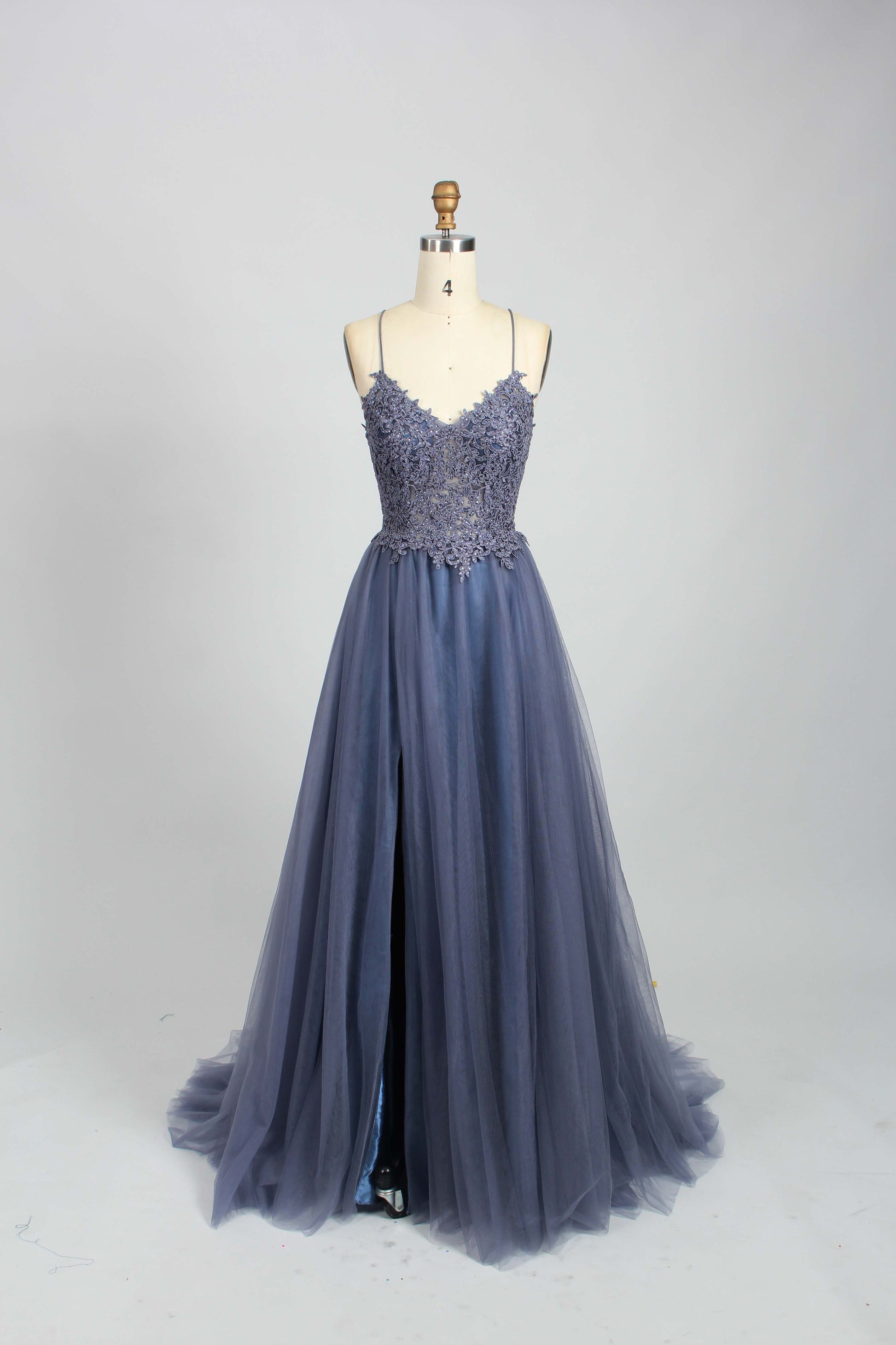 A mannequin showcases a dark - green tulle gown. It has thin spaghetti straps, a lace - detailed bodice, and a voluminous, flowing skirt. The elegant design, with its romantic tulle and delicate lace, suits formal events like galas or weddings.