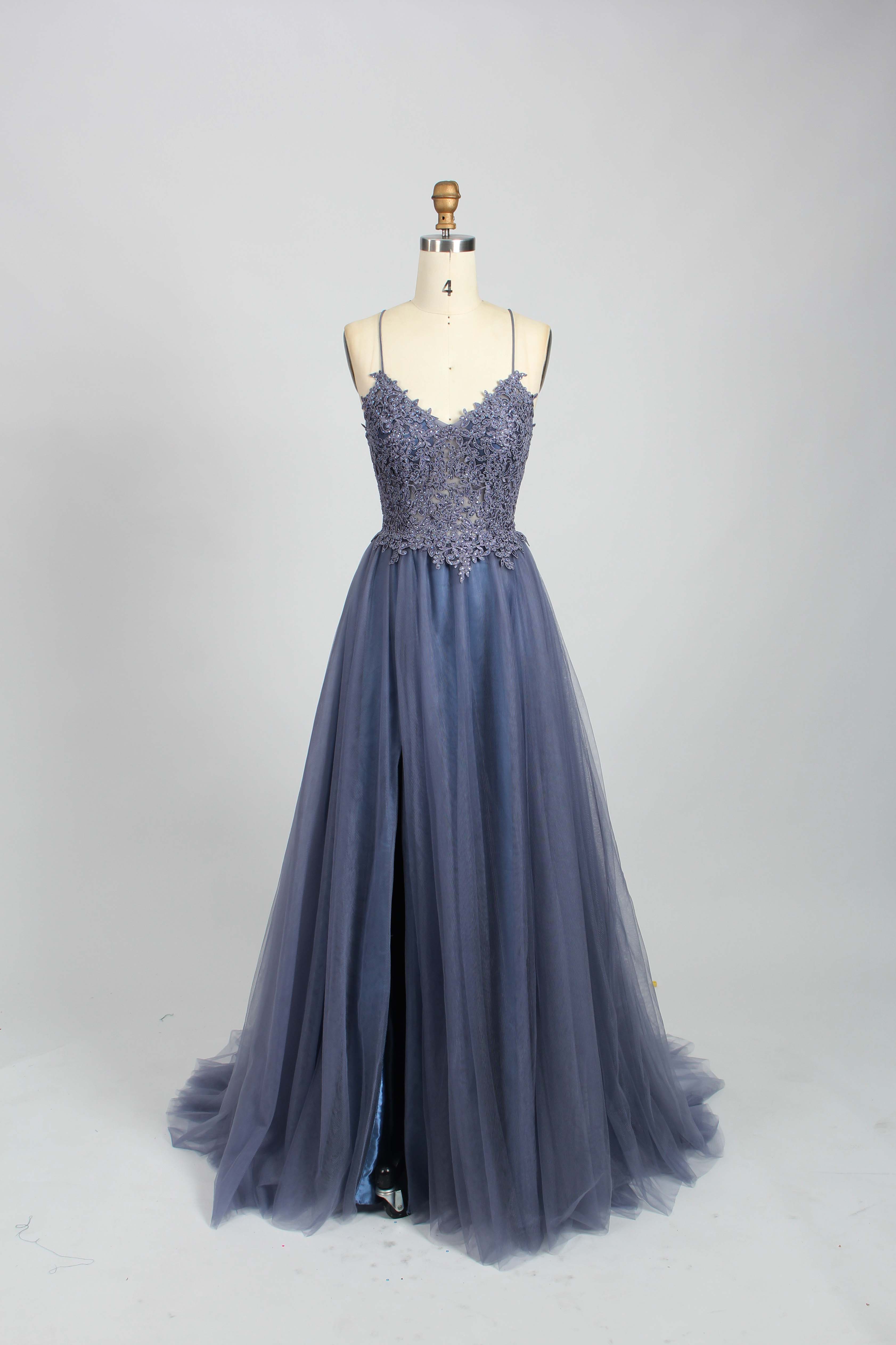 A mannequin showcases a dark - green tulle gown. It has thin spaghetti straps, a lace - detailed bodice, and a voluminous, flowing skirt. The elegant design, with its romantic tulle and delicate lace, suits formal events like galas or weddings.