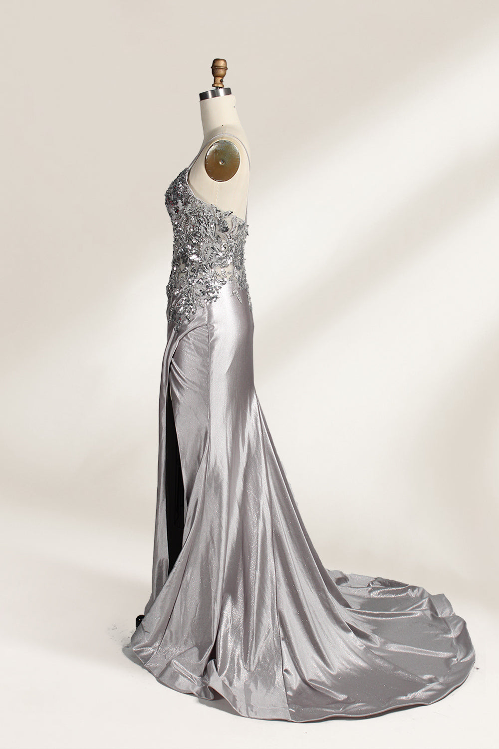 Photograph of a mannequin wearing a stunning, floor-length, navy blue satin evening gown. The gown features a deep V-back with thin straps and intricate sequin detailing along the back and neckline. The fitted bodice gradually flares into a flowing, elegant train. The mannequin stands against a plain, light beige backdrop, highlighting the gown's luxurious texture and shimmering finish. The gown exudes sophistication and glamour, ideal for formal events.5
