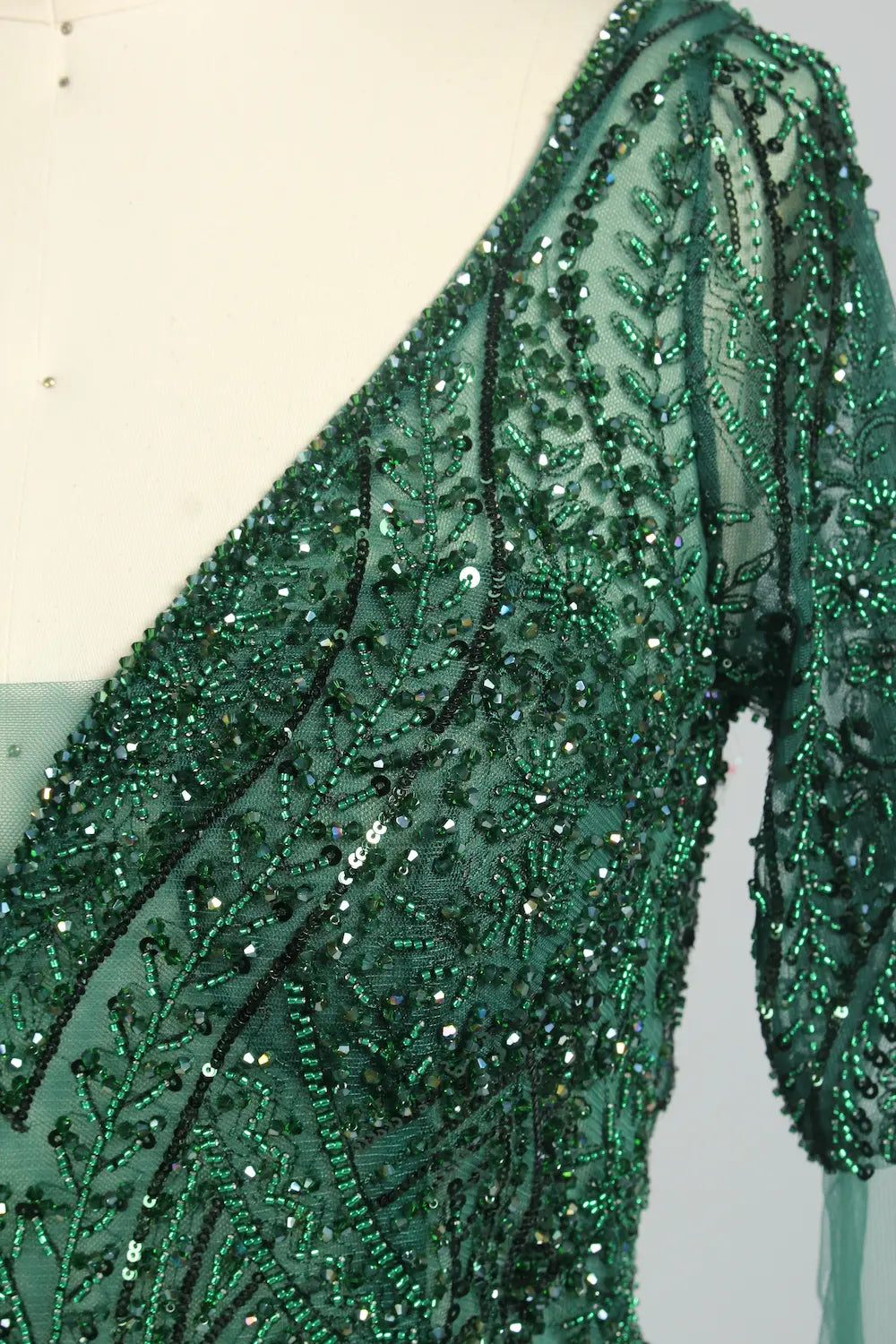 Close-up of dark green beaded sequin cape sleeve on embellished V-neck dress
