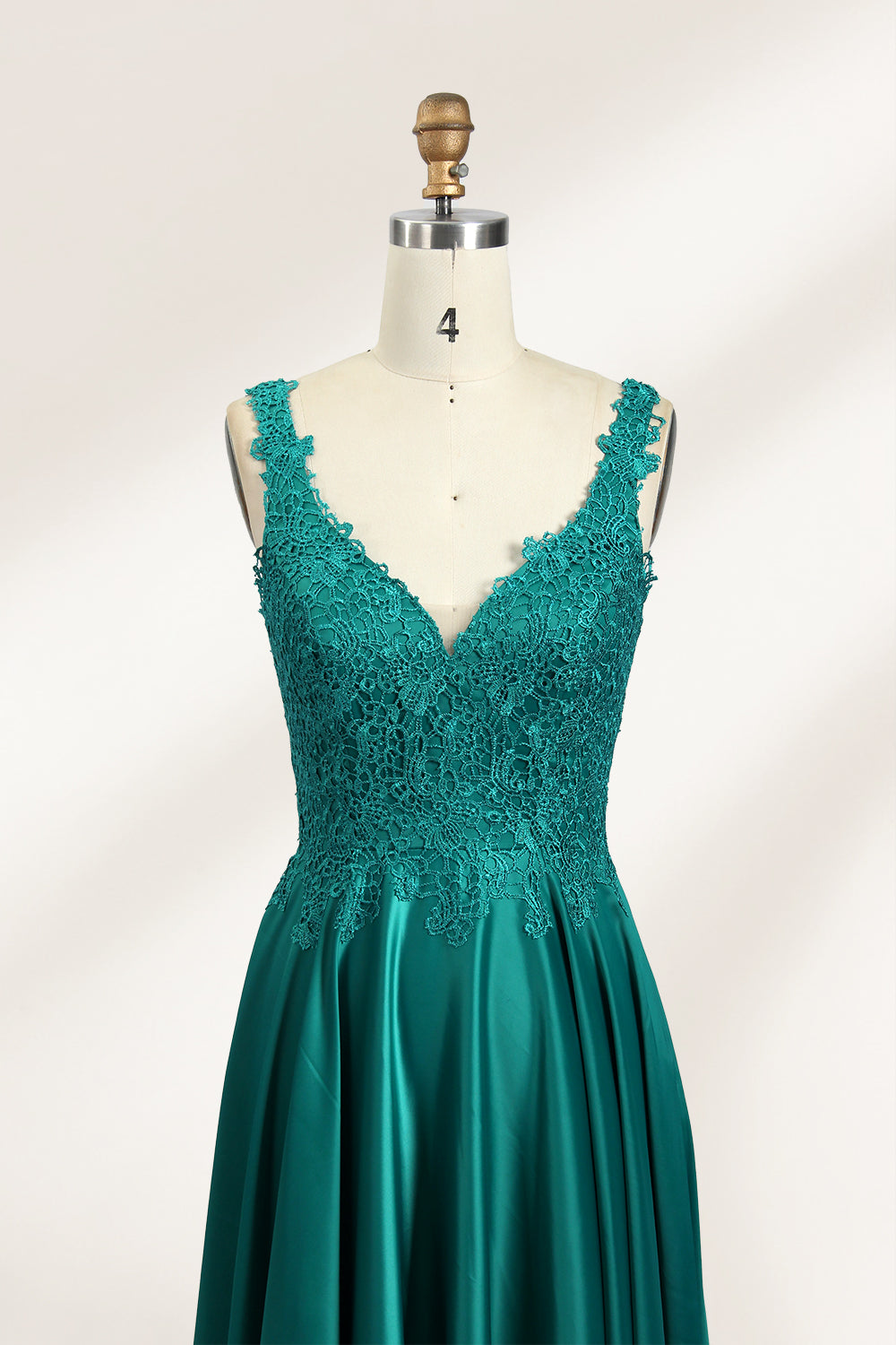 Photograph of a mannequin showcasing a teal, floor-length evening gown with a lace bodice and V-neckline. The gown features a fitted waist and a full, flowing skirt. The mannequin is set against a plain, light-colored background, highlighting the dress's elegant and luxurious design.03