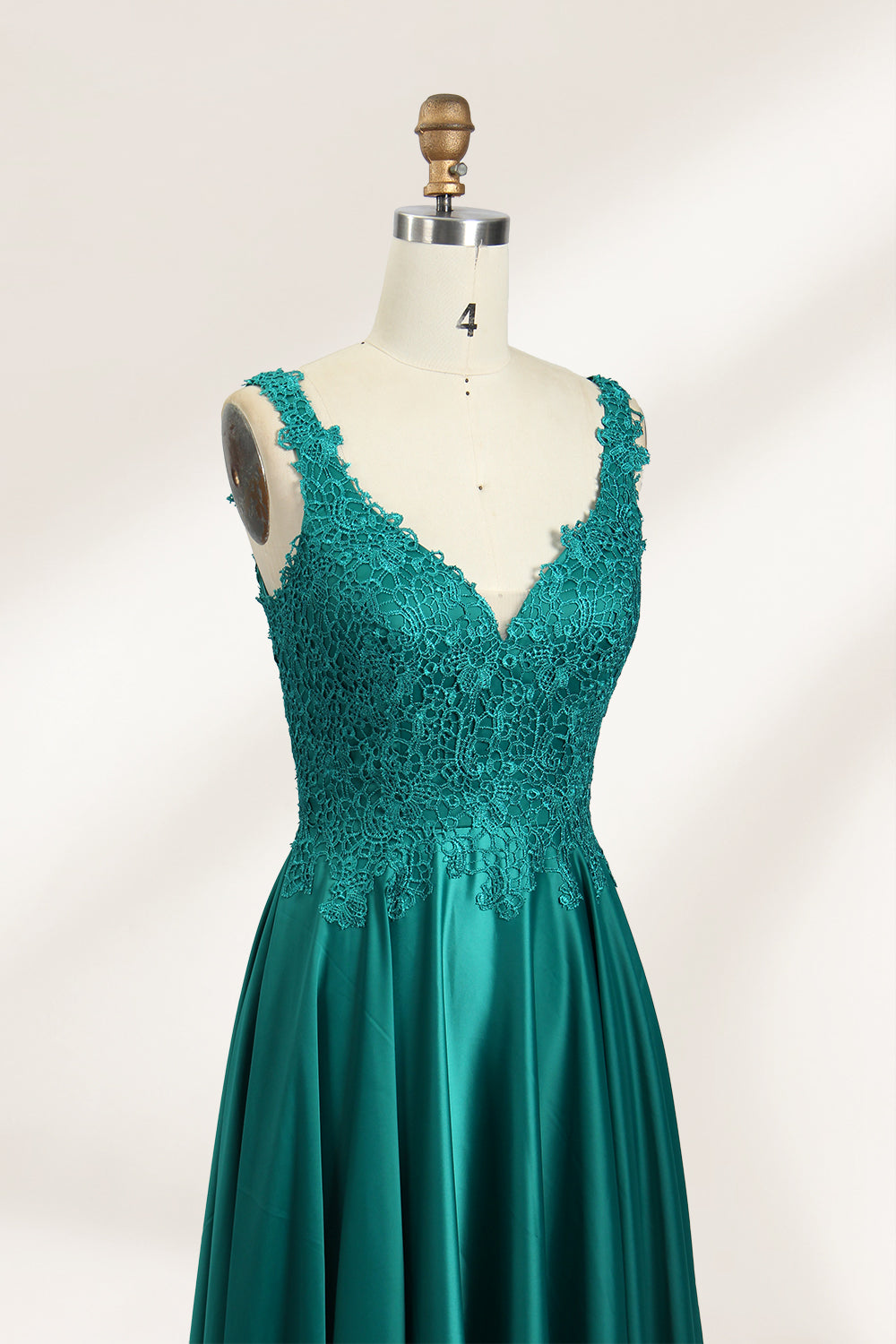 Photograph of a mannequin showcasing a teal, floor-length evening gown with a lace bodice and V-neckline. The gown features a fitted waist and a full, flowing skirt. The mannequin is set against a plain, light-colored background, highlighting the dress's elegant and luxurious design.05