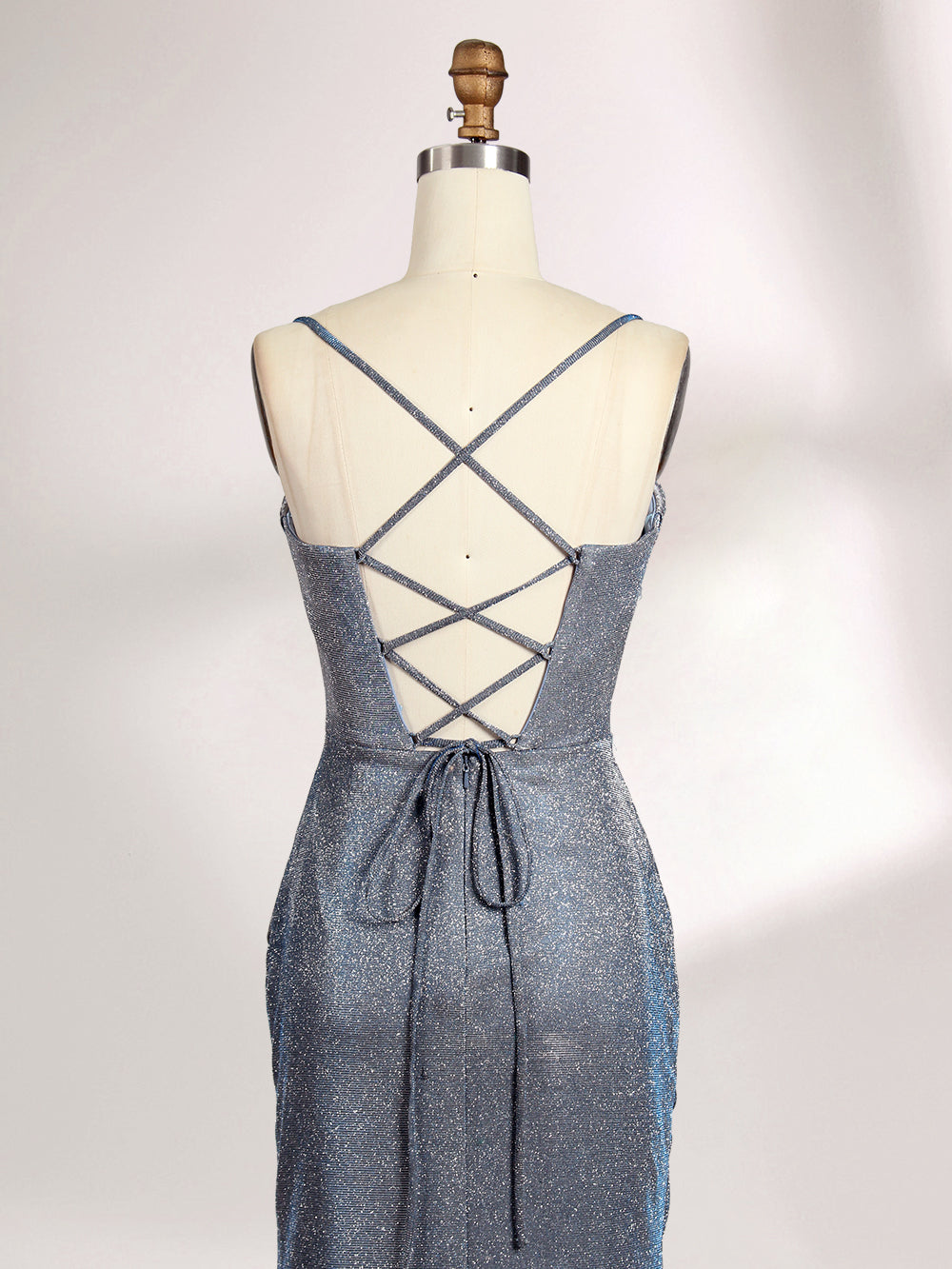 A woman stands against a light background, wearing a light - blue, shimmering gown. It has thin spaghetti straps, a cowl neckline, and a high side slit. The glittery fabric and elegant silhouette, paired with strappy heels, exude glamour, perfect for formal events like galas or proms.