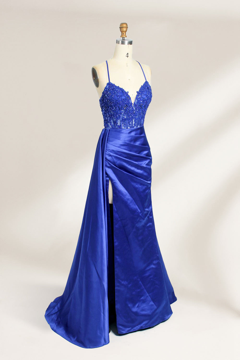 A mannequin showcases a royal - blue gown with thin straps. The bodice features intricate bead embroidery and sheer panels, while the skirt has a ruched design and a high side slit. The satin fabric and elegant details make it perfect for formal events like proms or galas, exuding sophistication.3