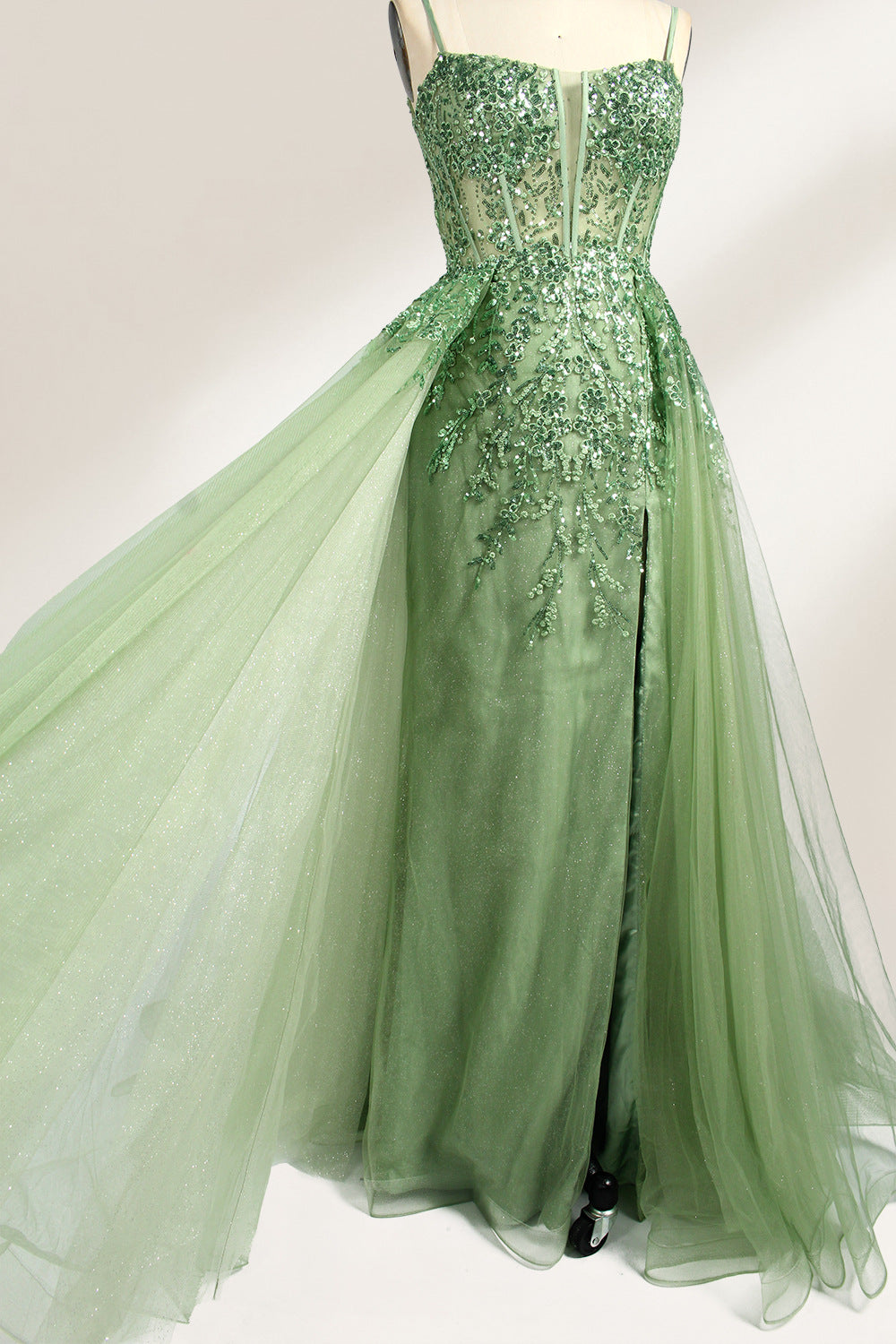 A photograph of a dark navy blue, floor-length evening gown displayed on a dress form. The gown features intricate floral embroidery in shades of purple and pink on the bodice, transitioning to a sheer, sparkling tulle skirt. The bodice is fitted with spaghetti straps, and the dress form is positioned against a plain, off-white background, highlighting the gown's elegant and luxurious design.7