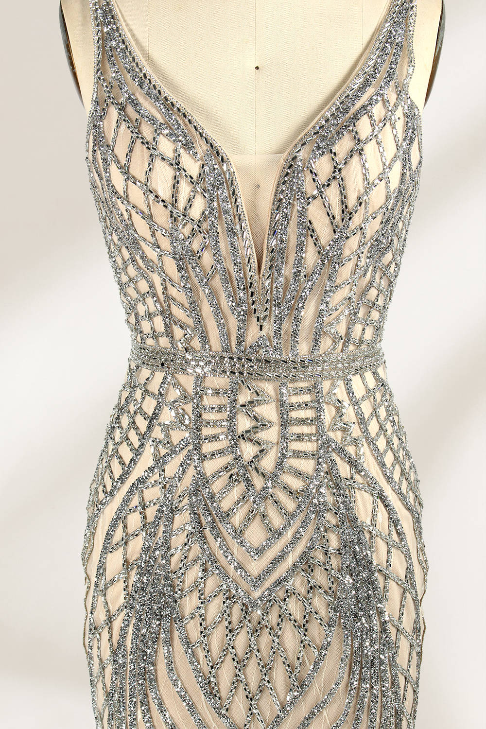 Against a light - hued backdrop, a mannequin displays a nude - toned tulle gown featuring silver beaded embellishments. It has thin straps, a deep V - neckline, and a mermaid - shaped skirt. The detailed beadwork weaves sophistication, perfect for formal dinners or weddings, where the beaded elegance complements the occasion.6