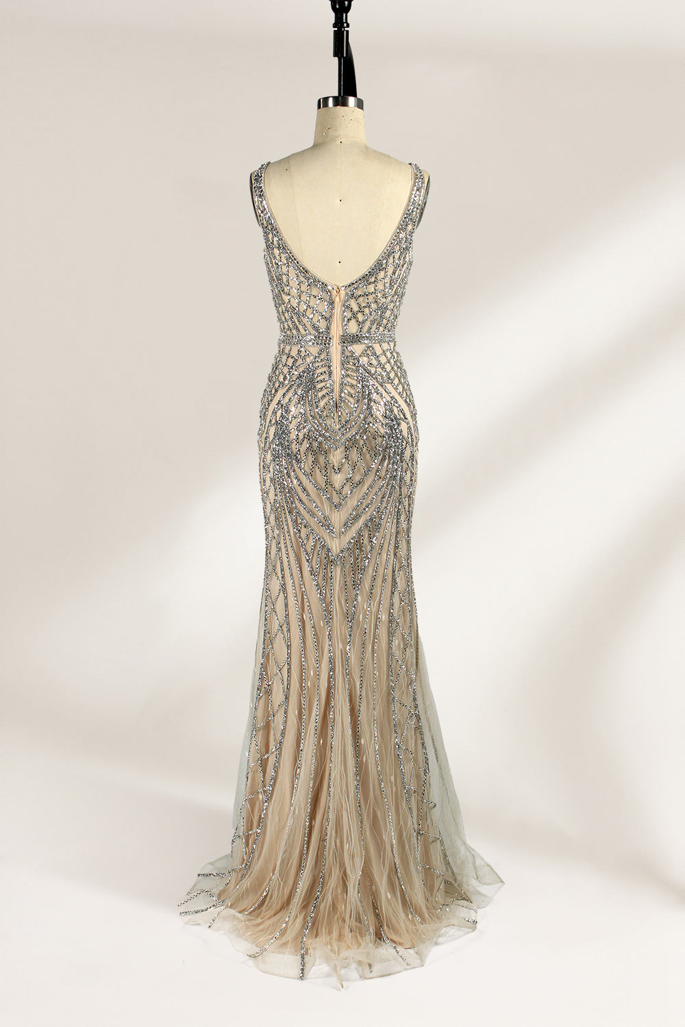 Against a light - hued backdrop, a mannequin displays a nude - toned tulle gown featuring silver beaded embellishments. It has thin straps, a deep V - neckline, and a mermaid - shaped skirt. The detailed beadwork weaves sophistication, perfect for formal dinners or weddings, where the beaded elegance complements the occasion.2