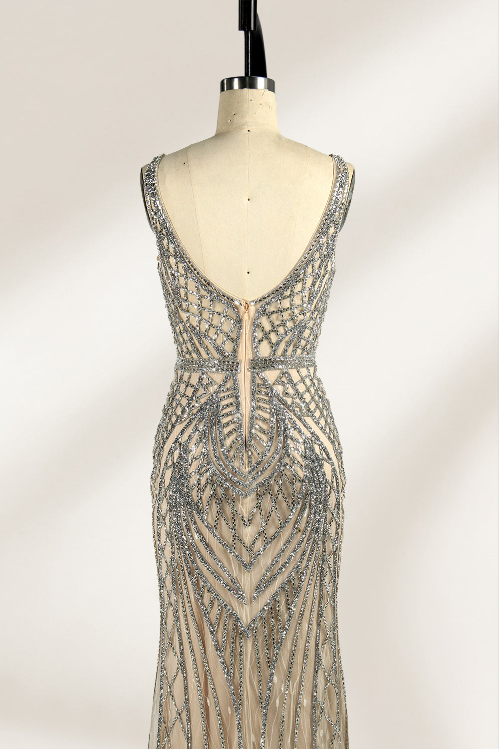 Against a light - hued backdrop, a mannequin displays a nude - toned tulle gown featuring silver beaded embellishments. It has thin straps, a deep V - neckline, and a mermaid - shaped skirt. The detailed beadwork weaves sophistication, perfect for formal dinners or weddings, where the beaded elegance complements the occasion.5