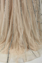 Against a light - hued backdrop, a mannequin displays a nude - toned tulle gown featuring silver beaded embellishments. It has thin straps, a deep V - neckline, and a mermaid - shaped skirt. The detailed beadwork weaves sophistication, perfect for formal dinners or weddings, where the beaded elegance complements the occasion.3