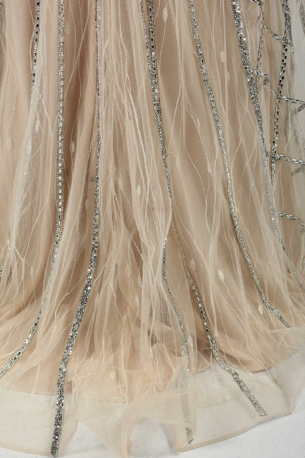 Against a light - hued backdrop, a mannequin displays a nude - toned tulle gown featuring silver beaded embellishments. It has thin straps, a deep V - neckline, and a mermaid - shaped skirt. The detailed beadwork weaves sophistication, perfect for formal dinners or weddings, where the beaded elegance complements the occasion.3