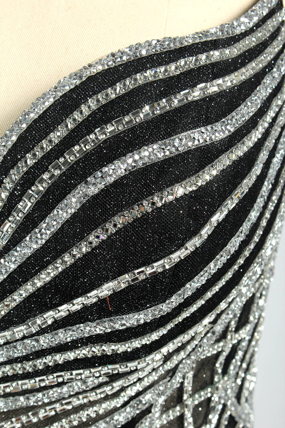Set against a light background, a mannequin presents a black tulle gown with silver - toned beaded embellishments. Thin straps, a sweetheart neckline, and a mermaid - style skirt complete the look. The geometric bead patterns add a touch of glamour, ideal for proms or formal events where the beaded artistry stands out.6